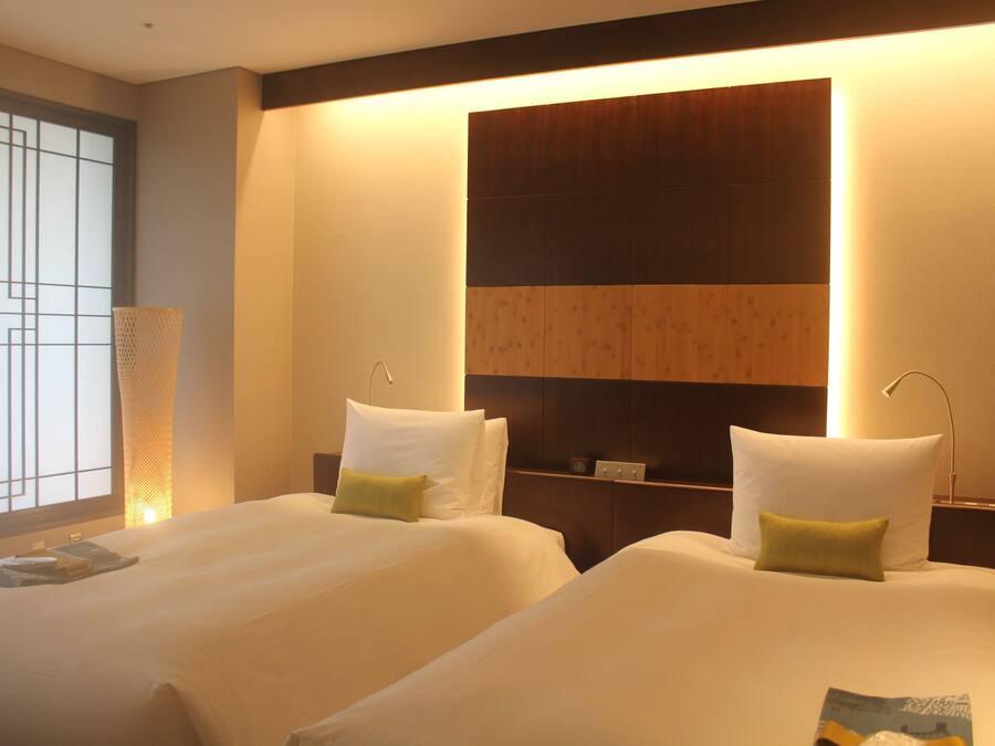 A hotel room with two beds, a large window with a view, and a wall-mounted shelf.