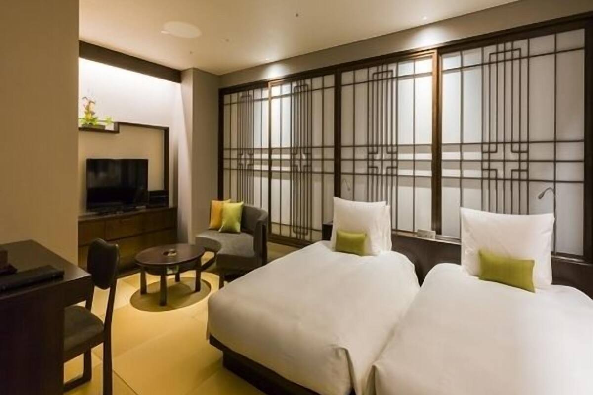 Une chambre d’hôtel comprenant un lit, deux chaises, une petite table, un téléviseur et un panneau décoratif mural.