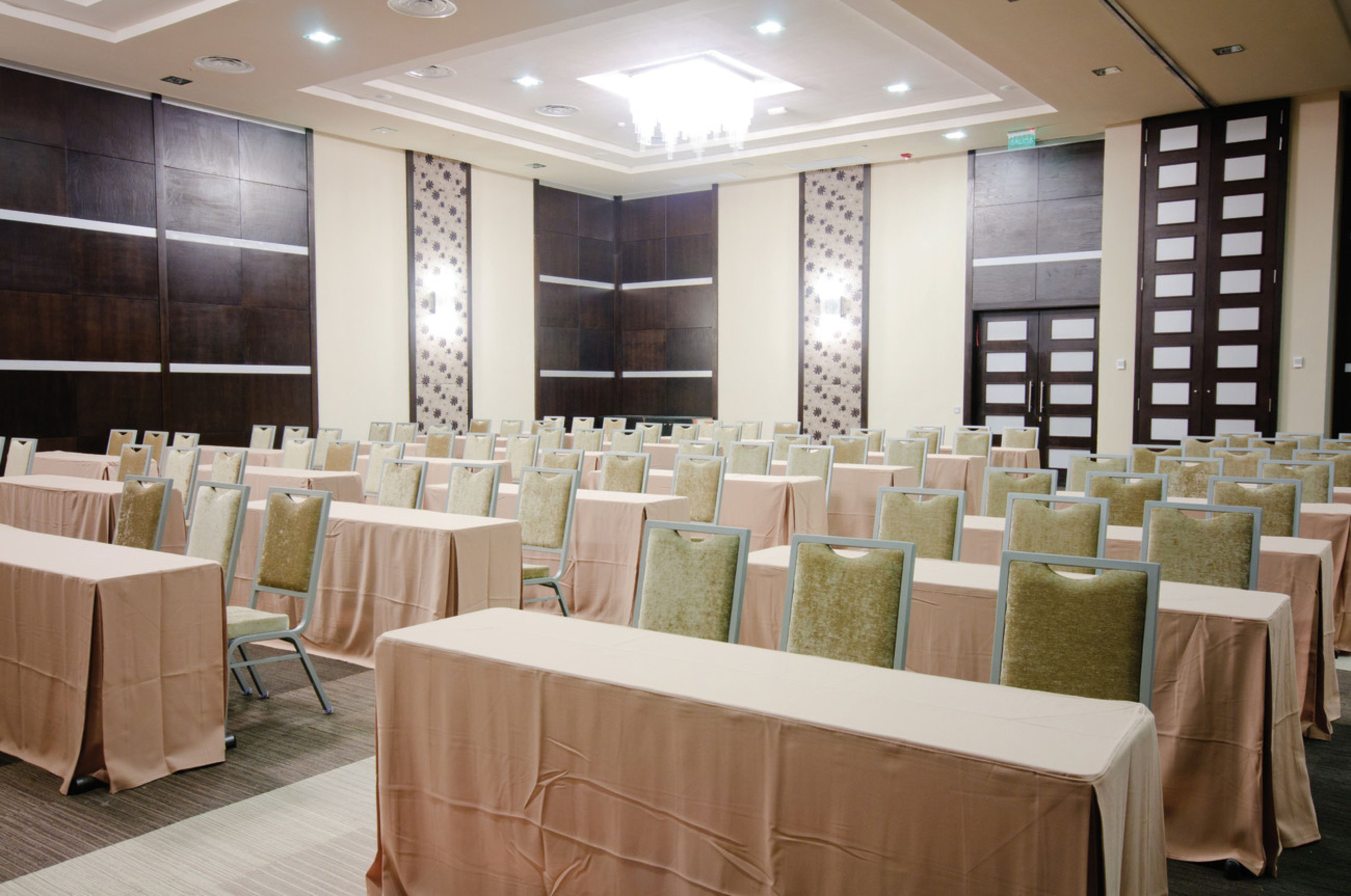 Un salón de conferencias con filas de mesas y sillas, ventanas amplias y un diseño de techo moderno.