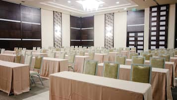 Un salón de conferencias con filas de mesas y sillas, ventanas amplias y un diseño de techo moderno.