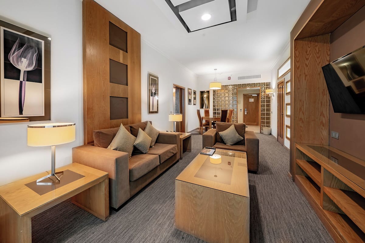 Una habitación de hotel moderna con un conjunto de sofás, una mesa de centro, un televisor y una estantería.
