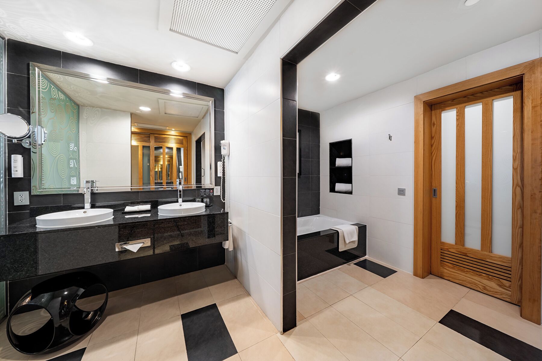 A modern bathroom with two sinks, a large mirror, and a wooden door.