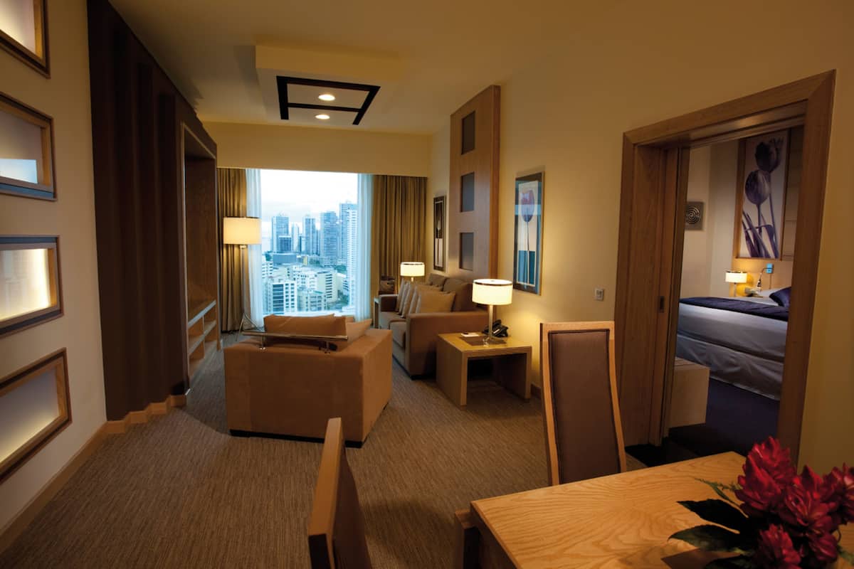 Habitación de hotel con vista a la ciudad, una cama, un escritorio, una silla, una mesa y una lámpara.