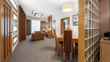 A hotel room with a seating area, a desk, a lamp, and a bookshelf.