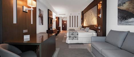 Una habitación de hotel moderna con un sofá, un escritorio y una cama. Hay luces empotradas en la pared y un cuadro colgado.