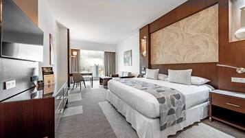 A modern hotel room with a large bed, a desk, a chair, and a TV.