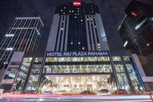 Fachada moderna de vidrio del Hotel Riu Plaza Panamá, con señalización iluminada.