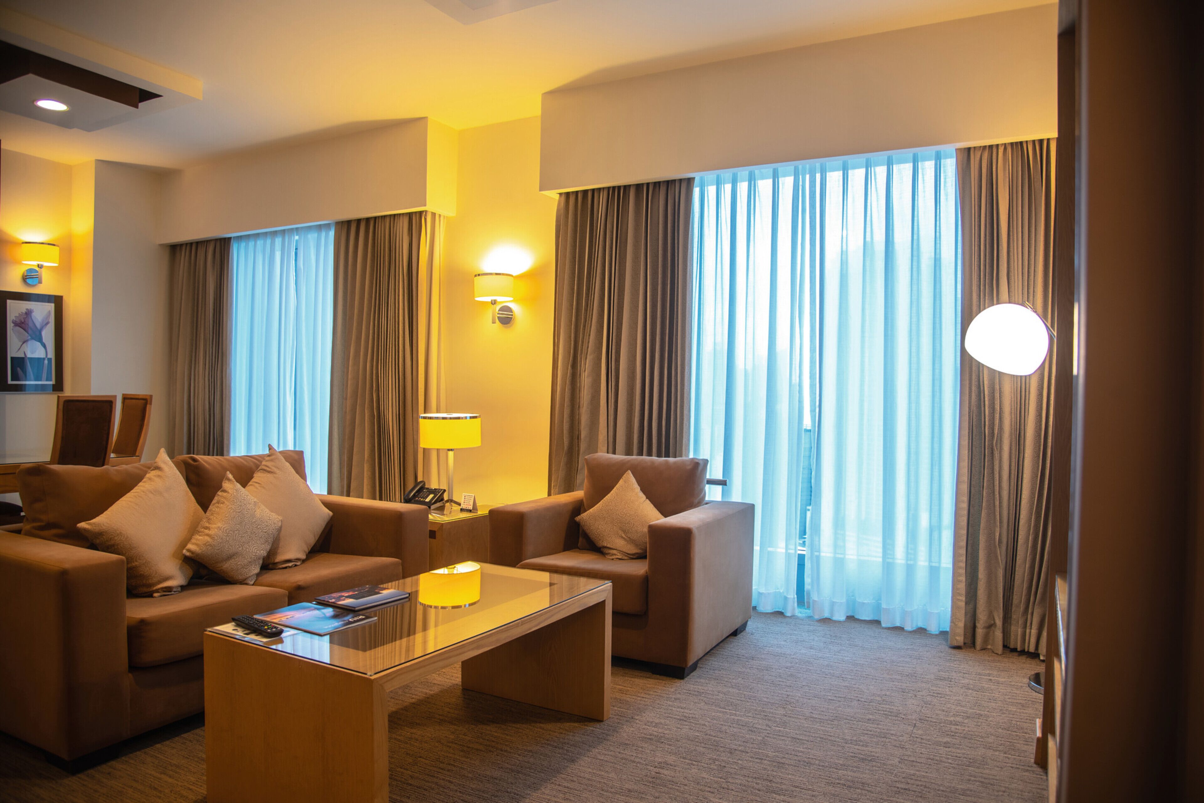 A hotel room with a sofa set, a coffee table, and a lamp.
