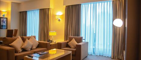 A hotel room with a sofa set, a coffee table, and a lamp.