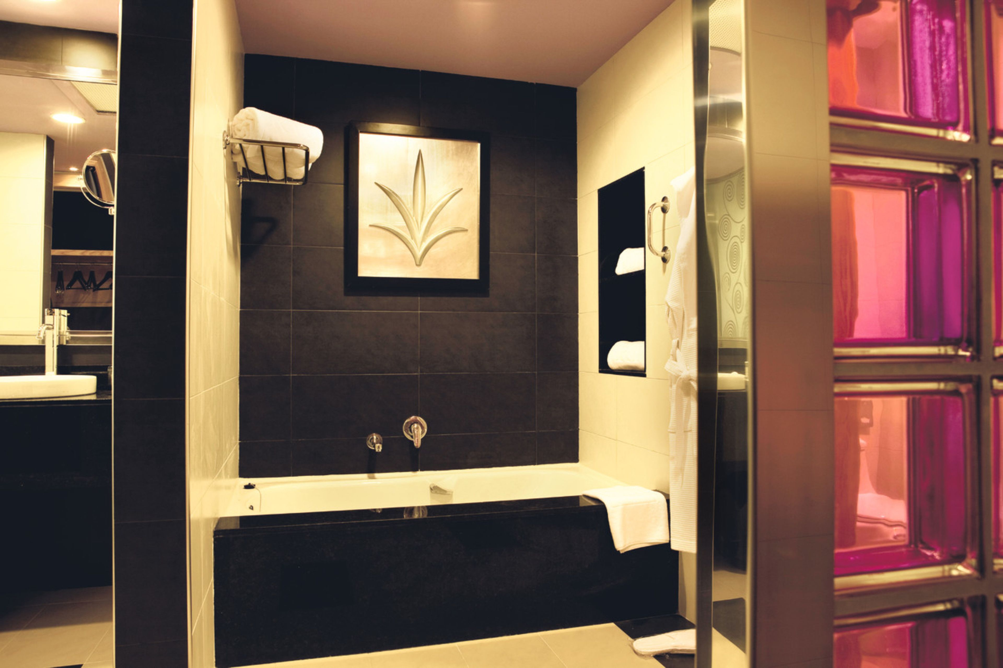 A modern bathroom with a black tiled wall, a white bathtub, and a framed artwork above the tub.