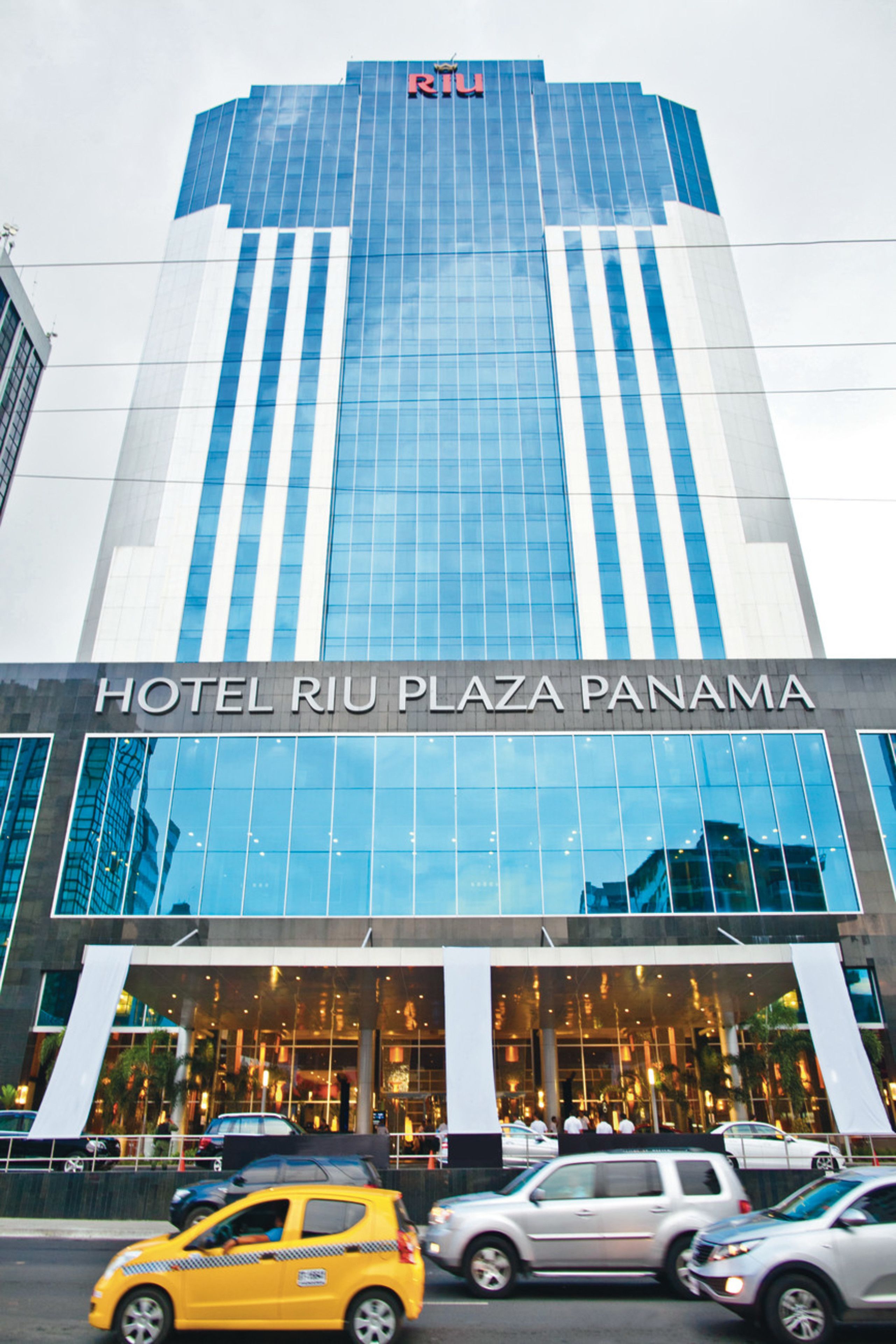 Un hôtel moderne avec une façade en verre et l’inscription « HOTEL RIU PLAZA PANAMA » bien visible.