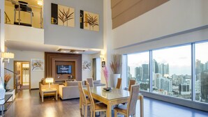 A modern hotel room with a dining area, a TV, and a city view.