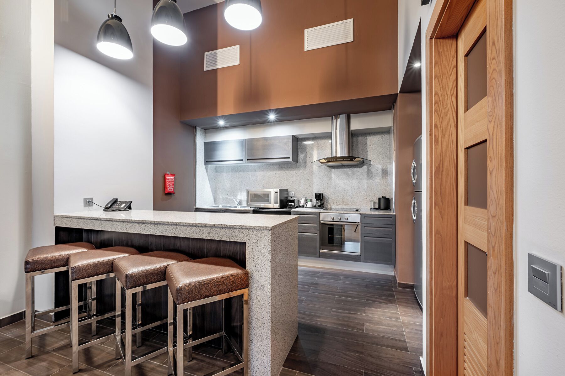 A modern kitchen with a central island, stainless steel appliances, and a wooden door.