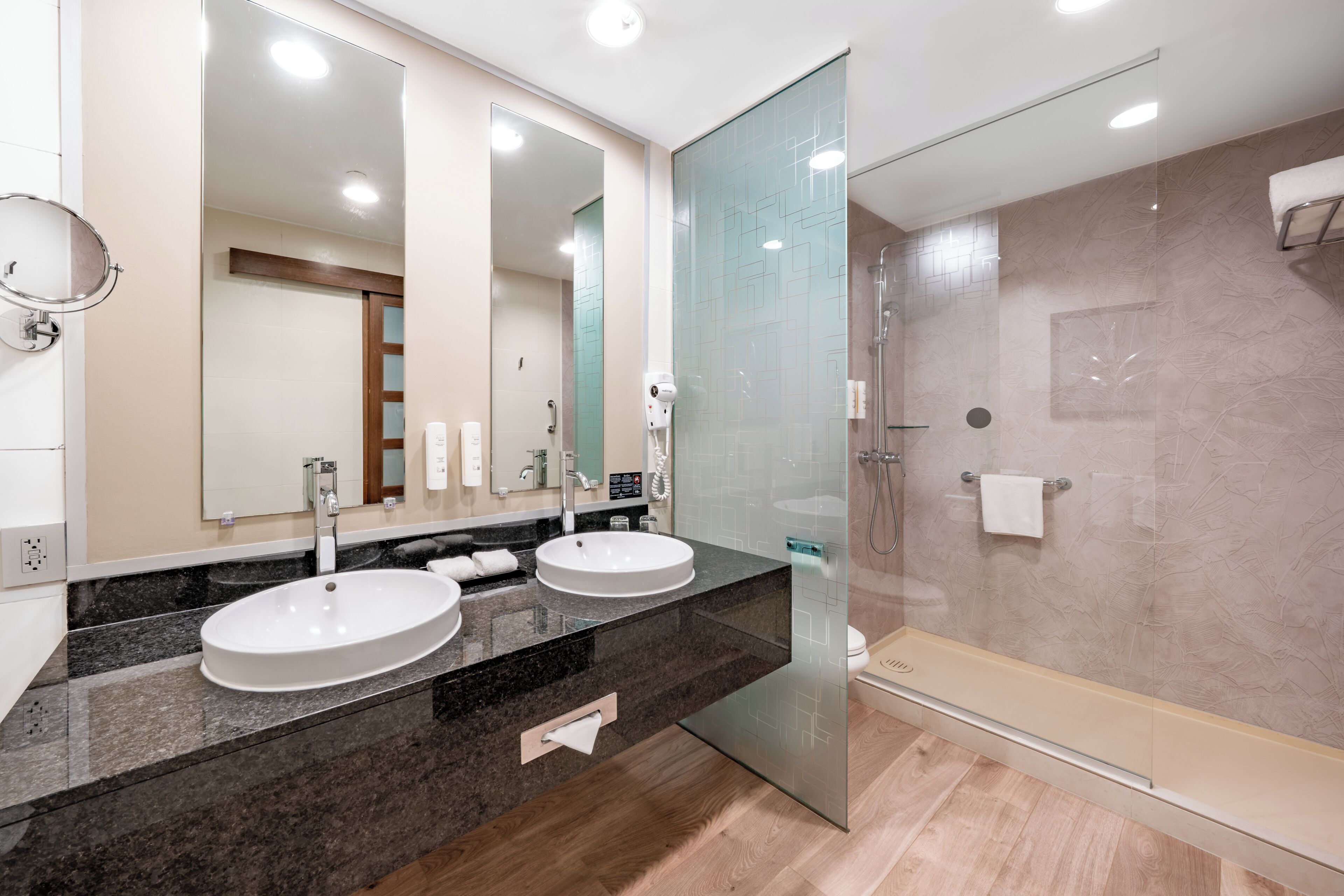 A modern bathroom with two sinks, a glass shower enclosure, and a large mirror.