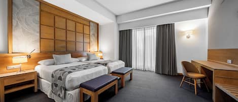 Habitación de hotel con una cama grande, dos mesitas de noche, un escritorio, una silla y un amplio ventanal con cortinas.