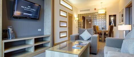 Una habitación de hotel moderna con televisión de pantalla plana, una mesa de centro de vidrio y una zona de estar con sofá y sillones.