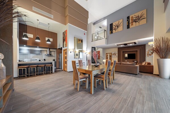 A modern kitchen with a central island, a dining area with a glass table, and a living room with a sofa and TV.