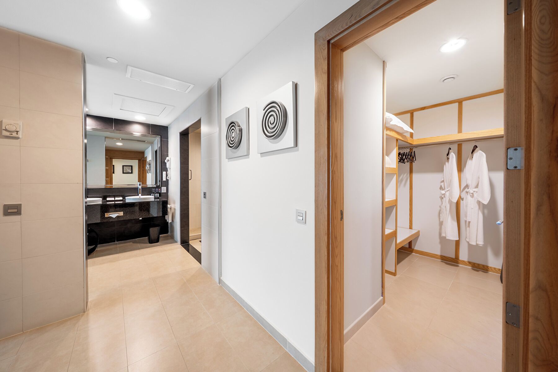 Un pasillo moderno de hotel con baño, tocador y vestidor con batas.