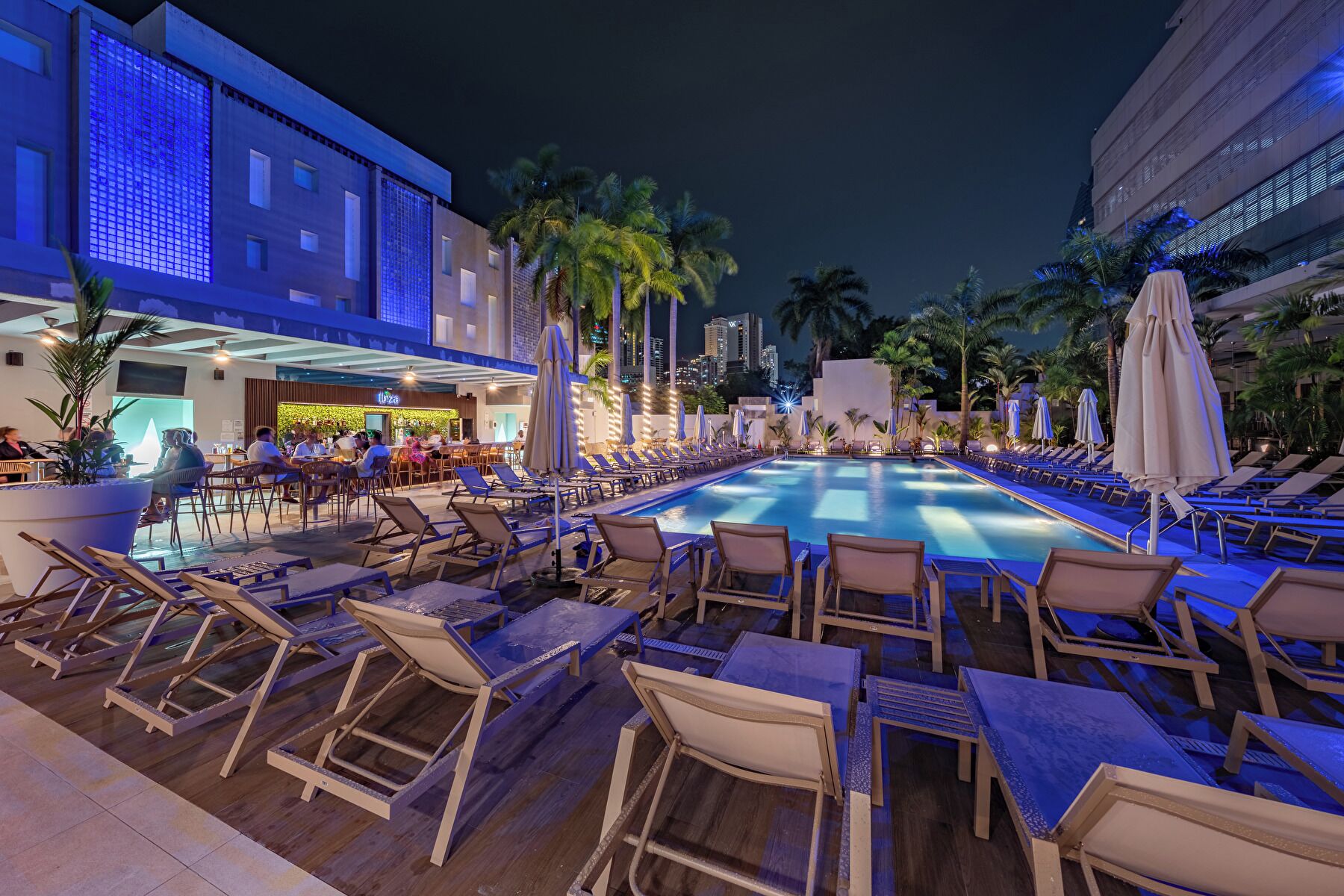 A poolside area with lounge chairs and umbrellas, a bar, and a building with a modern design.
