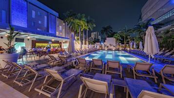 A poolside area with lounge chairs and umbrellas, a bar, and a building with a modern design.