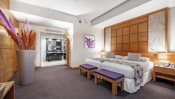 Quarto de hotel moderno com uma cama grande, duas mesas de cabeceira, um painel de cabeceira de madeira, uma janela ampla e um banheiro visível através de uma porta aberta.