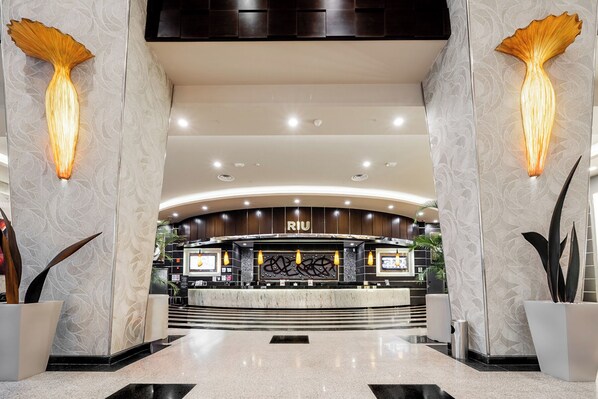 A modern hotel lobby with a reception desk, a curved ceiling, and decorative wall sconces.