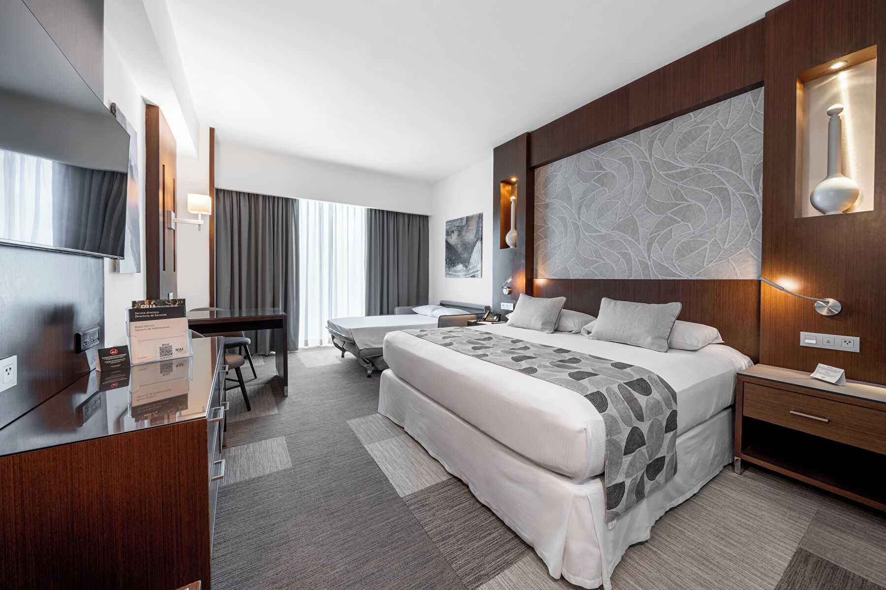 A modern hotel room with a large bed, a desk, and a TV.