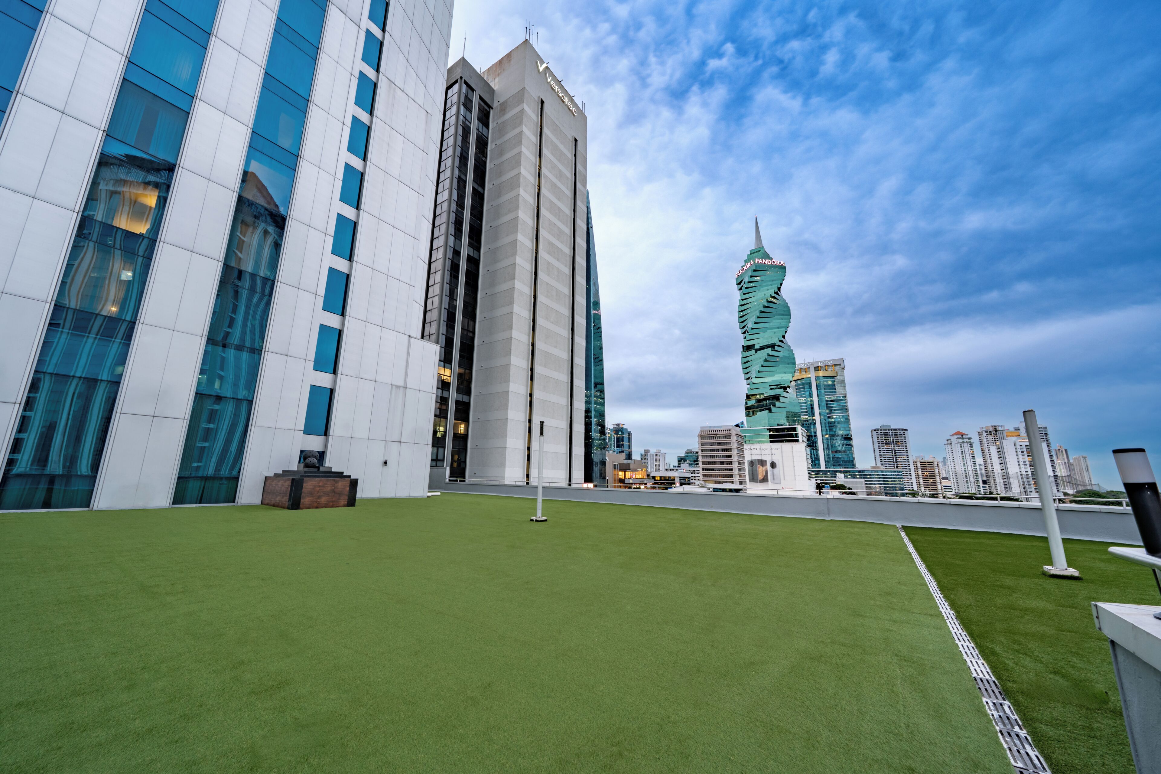 A rooftop with artificial grass, modern buildings, and a clear sky.
