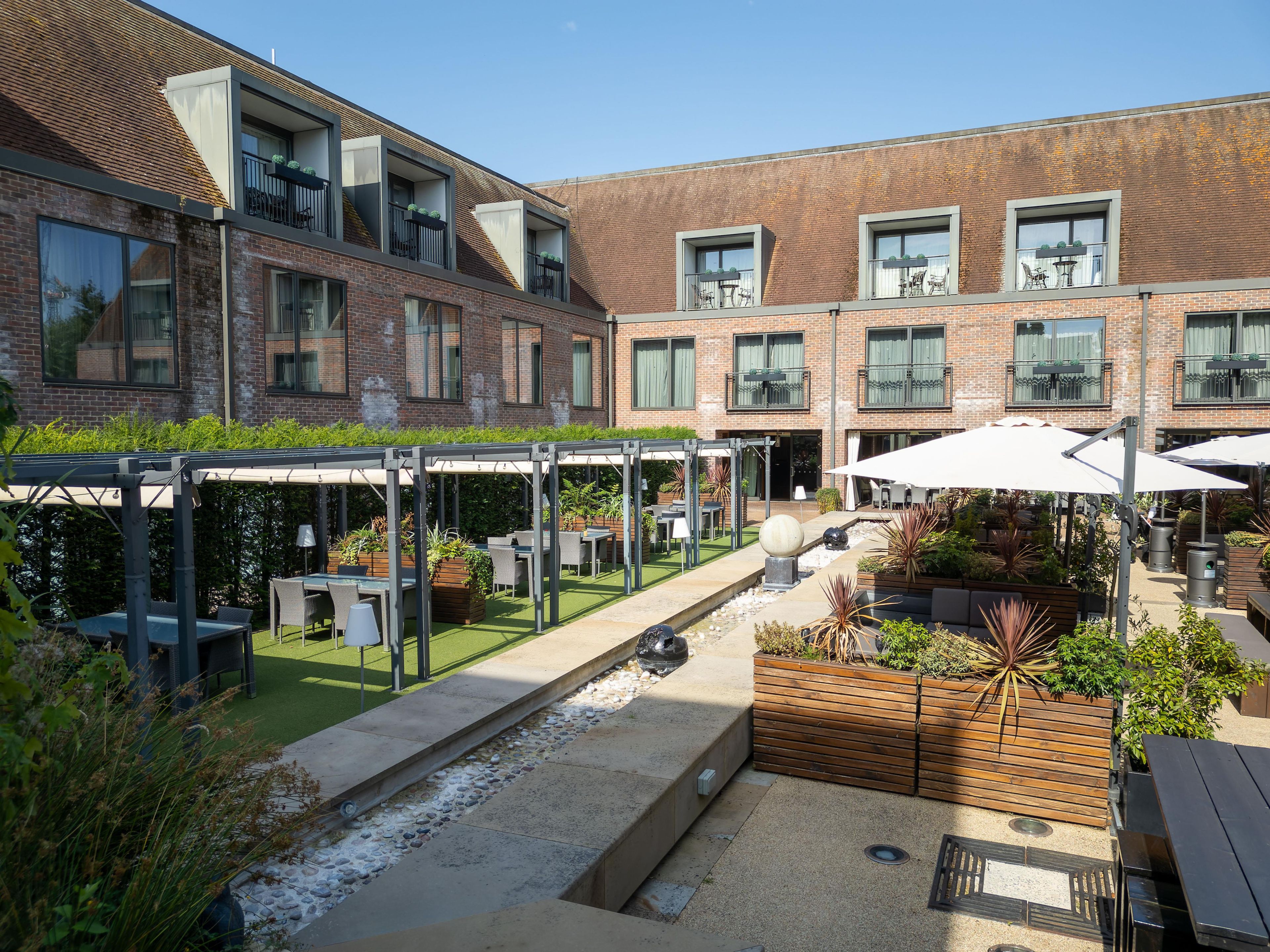 A courtyard with outdoor seating, a water feature, and a brick building with multiple windows.