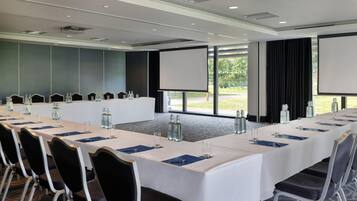 A conference room with a long table, chairs, a projector screen, and a view of the outdoors.