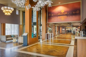 A hotel lobby with a reception desk, seating area, and a large window. - Hilton London Syon Park (Brentford)