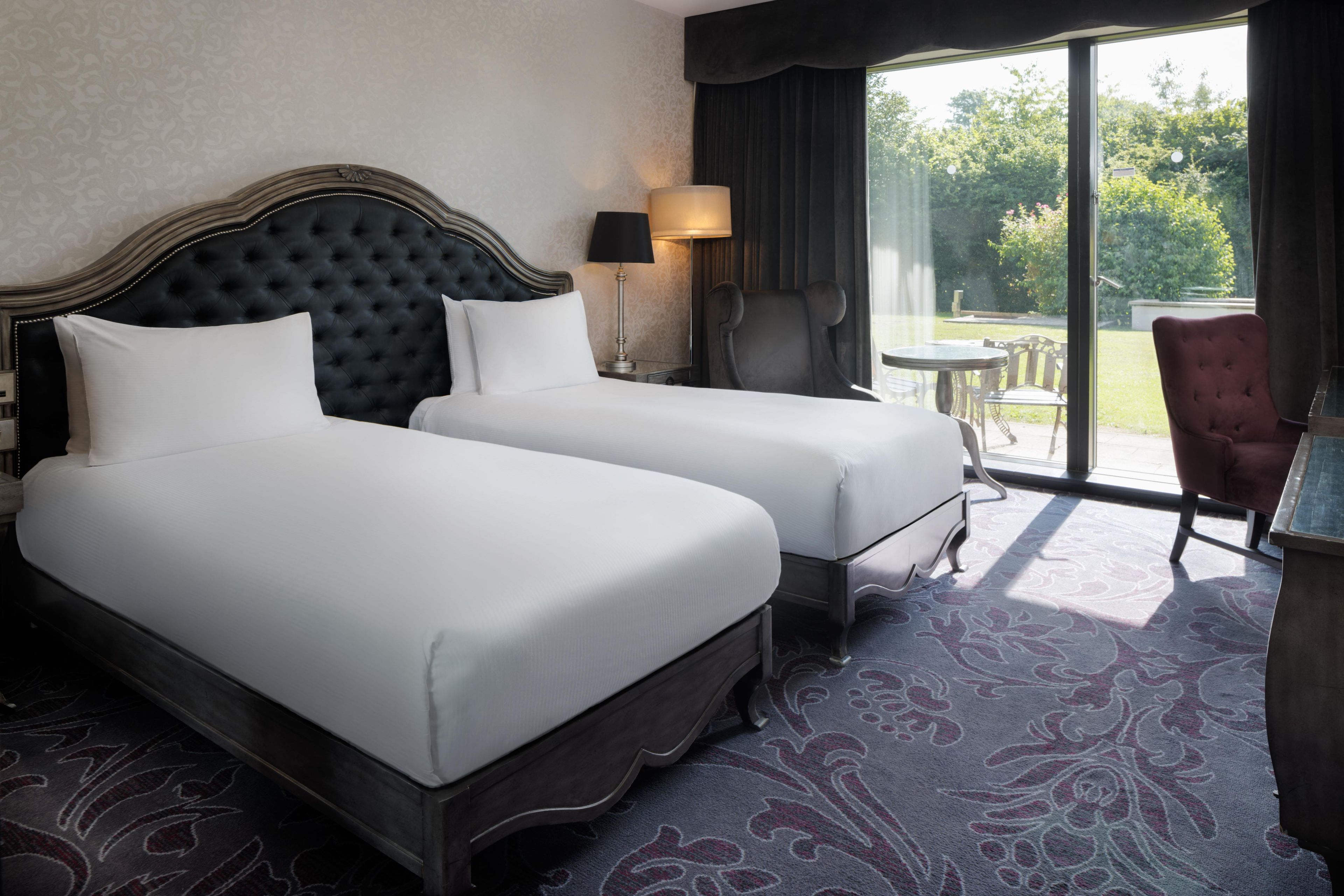 A hotel room with two beds, a sitting area with a table and chairs, and a view of the outdoors.