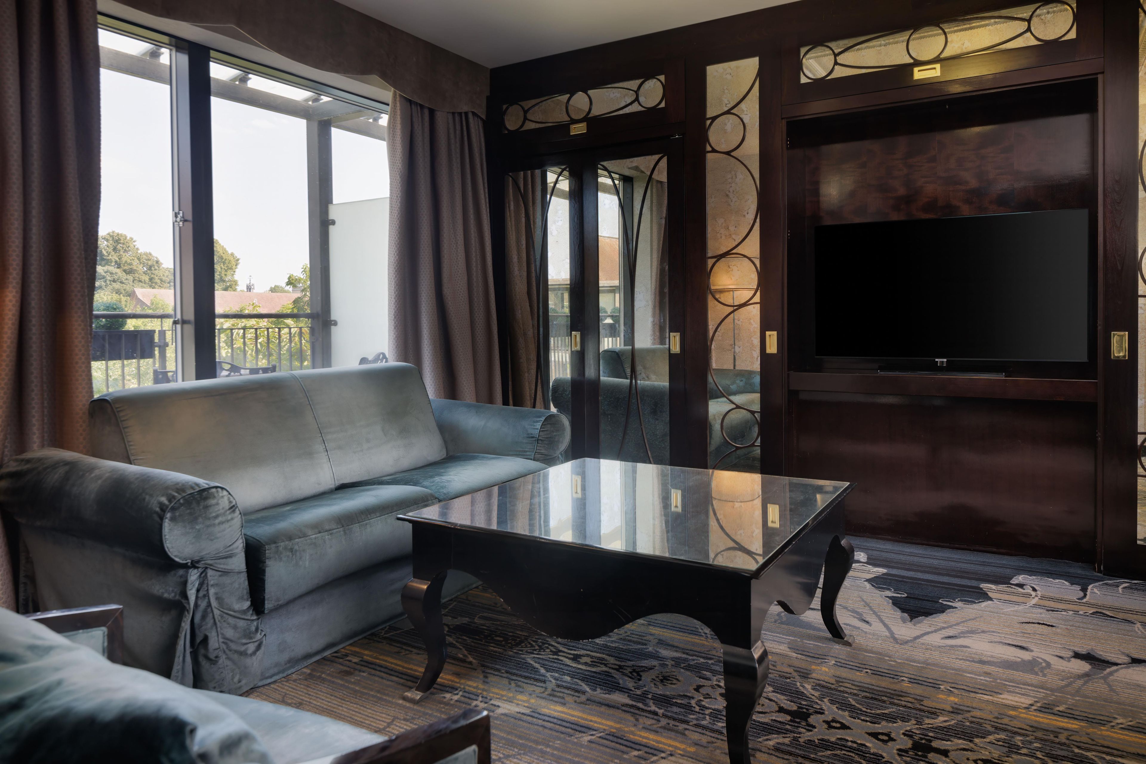A modern living room with a leather sofa, a glass coffee table, and a flat-screen TV mounted on a dark wooden wall.