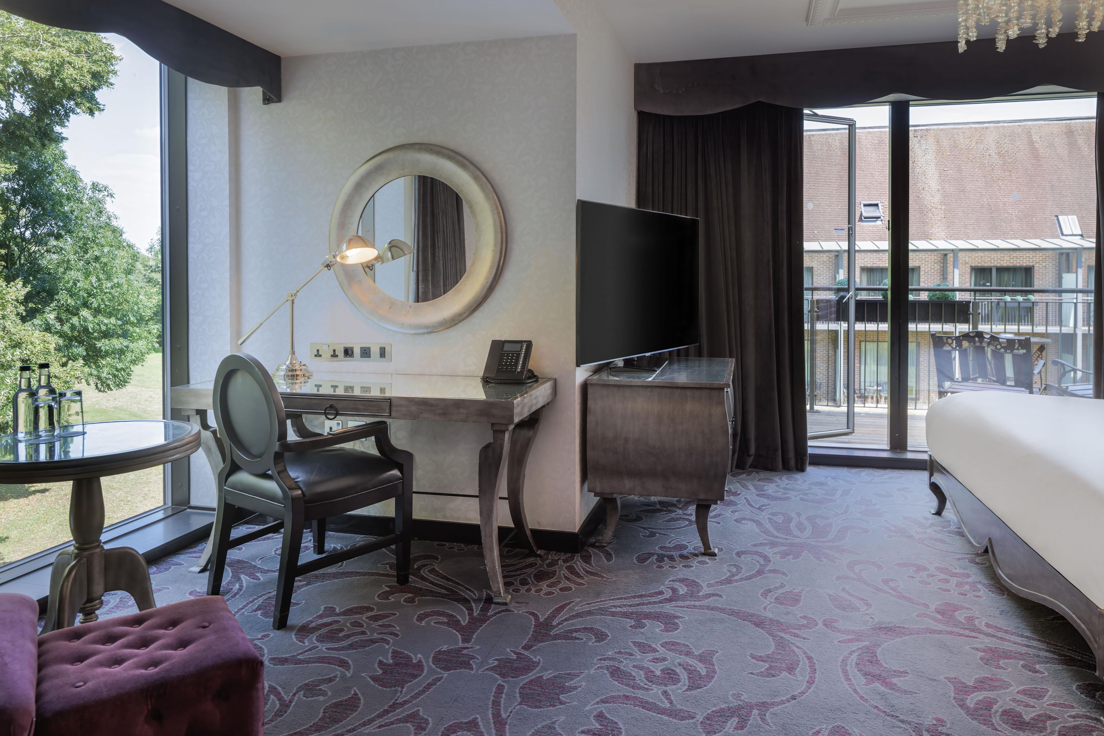 A hotel room with a desk, chair, bed, and a large window with a view of the outside.