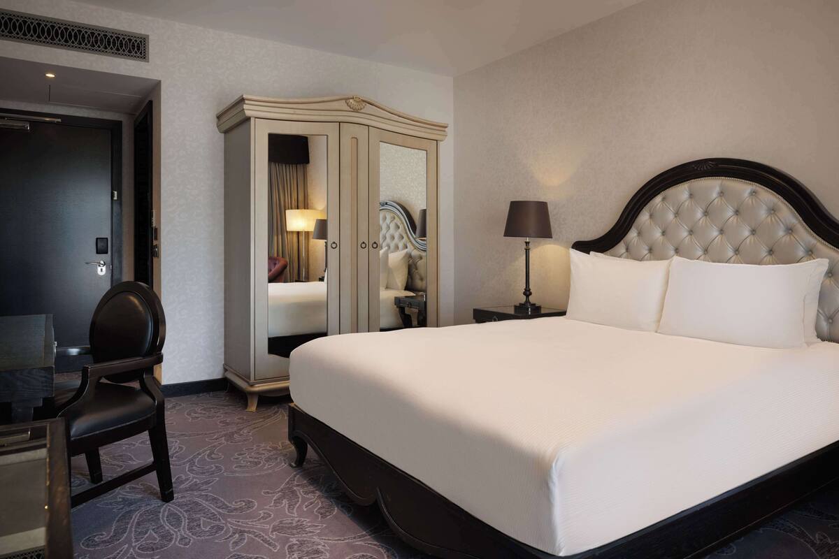 Quarto de hotel com uma cama grande, um guarda-roupa, uma escrivaninha e uma cadeira.
