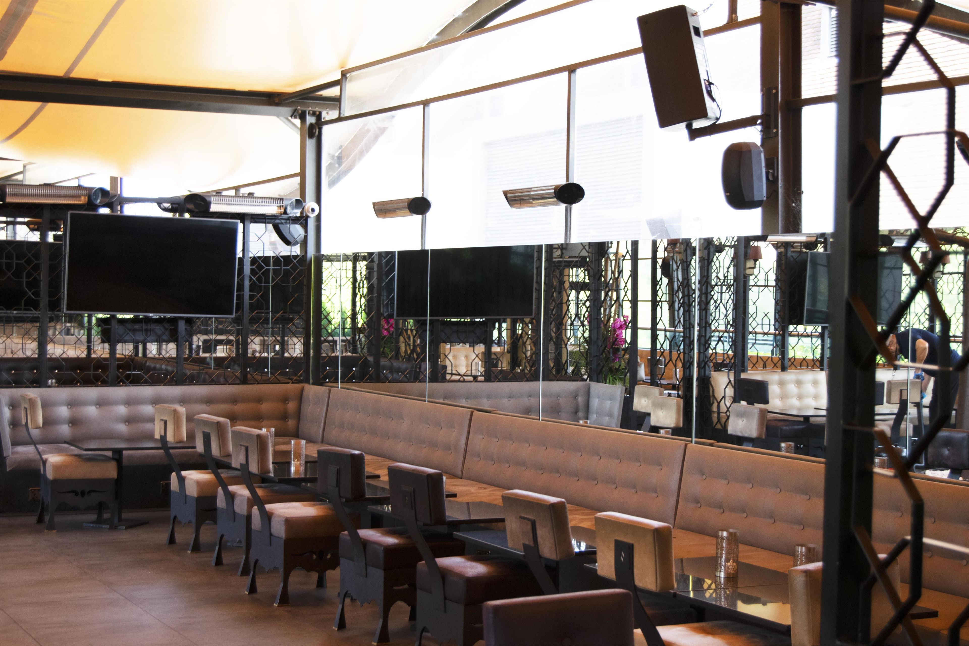 An outdoor seating area with tables and chairs, a large TV screen, and a canopy overhead.