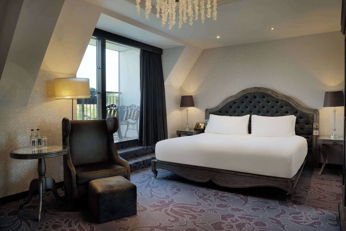 Quarto de hotel com uma cama grande, uma cadeira, uma mesa pequena e uma varanda com vista.