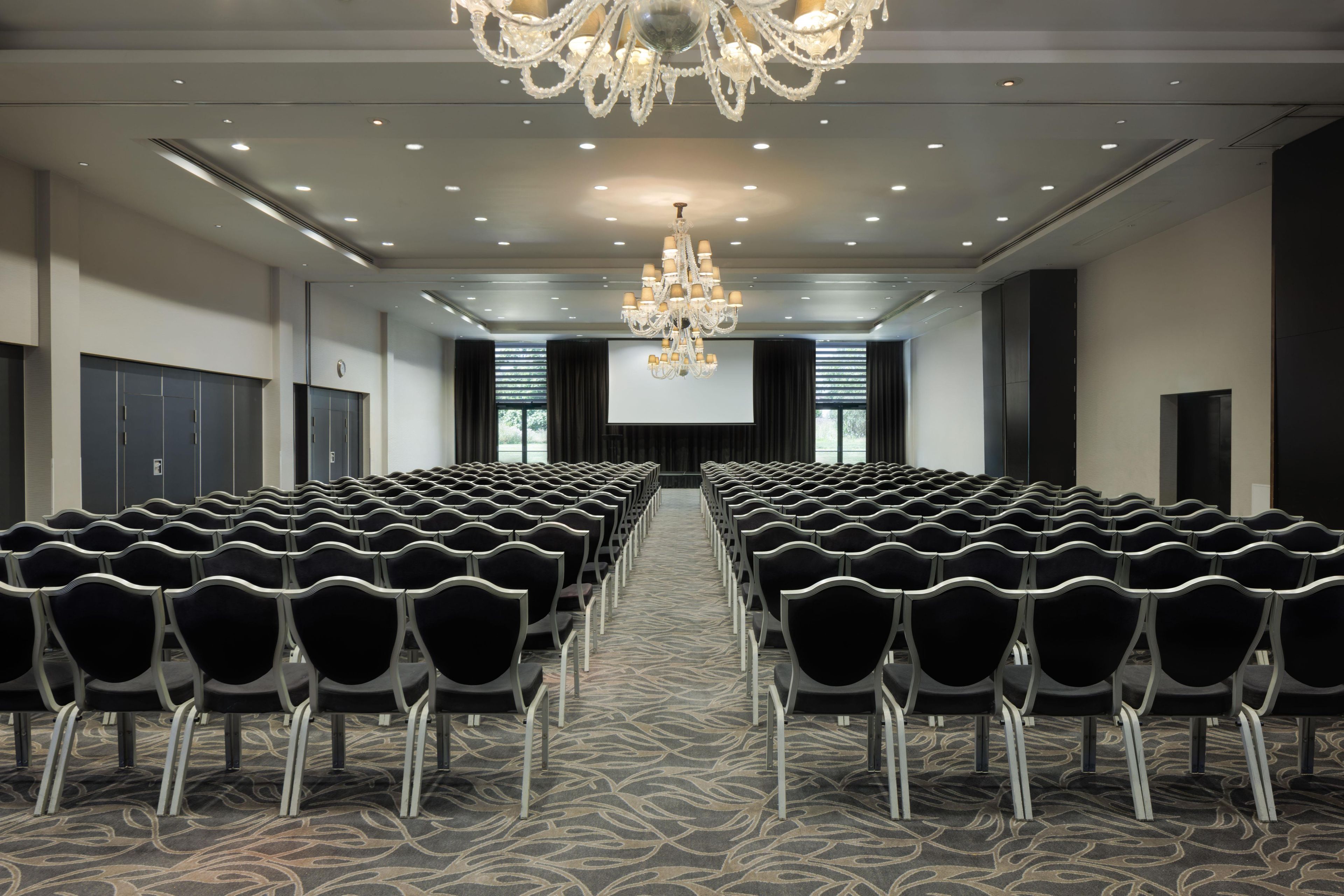 Un salón de conferencias con filas de sillas, una pantalla grande y una araña de cristal.