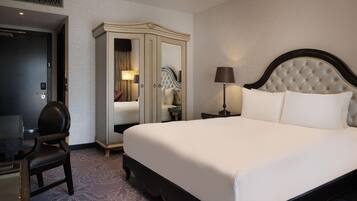 A hotel room with a large bed, a desk, a wardrobe, and a mirror.