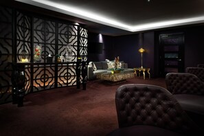 A modern living room with a dark color scheme, a sectional sofa, a coffee table, and decorative items. - Hilton London Syon Park (Brentford)