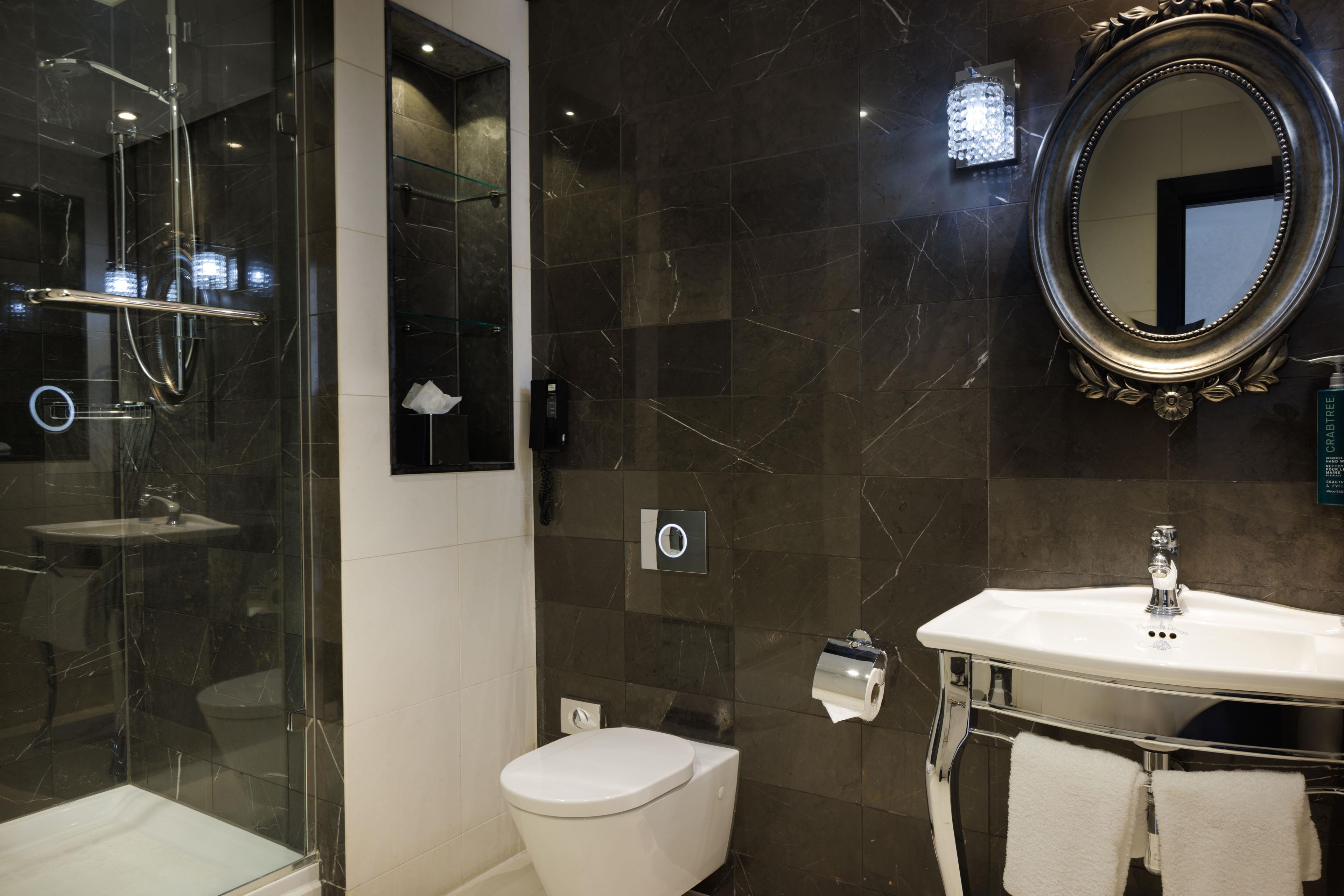 Un baño moderno con ducha envuelta en cristal, inodoro blanco, tocador con espejo y barra para toallas.