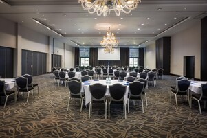 Un salón de conferencias con mesas redondas, sillas, una araña y una pantalla para proyector.