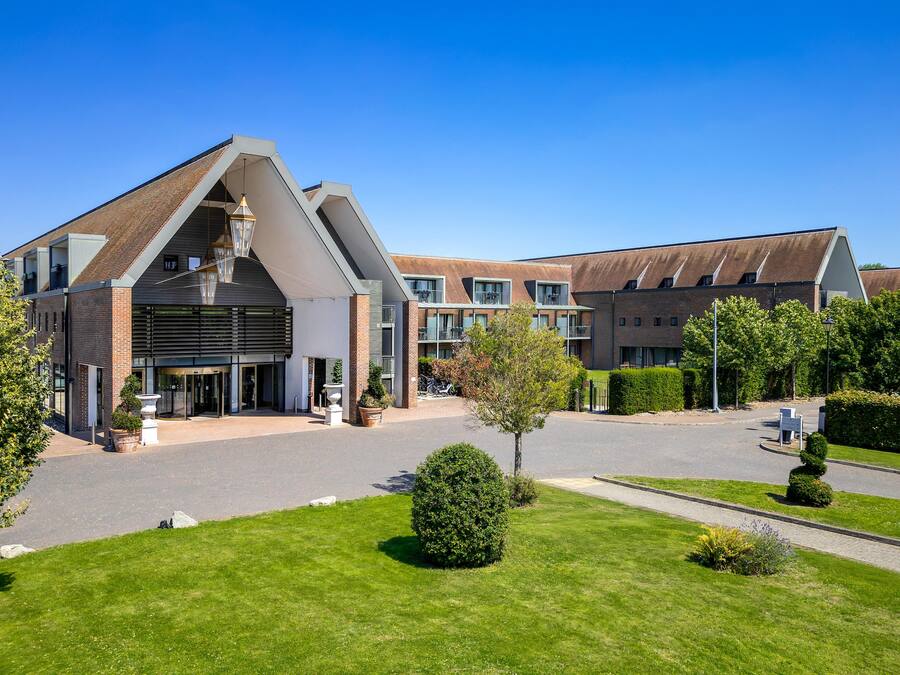 A modern hotel with a prominent entrance, multiple balconies, and a well-maintained lawn.