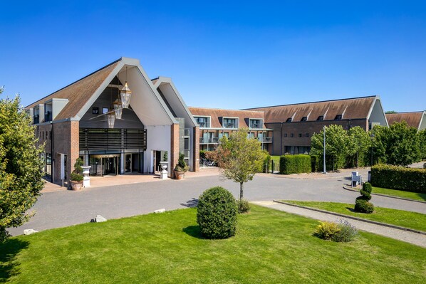 A modern hotel with a prominent entrance, multiple balconies, and a well-maintained lawn.