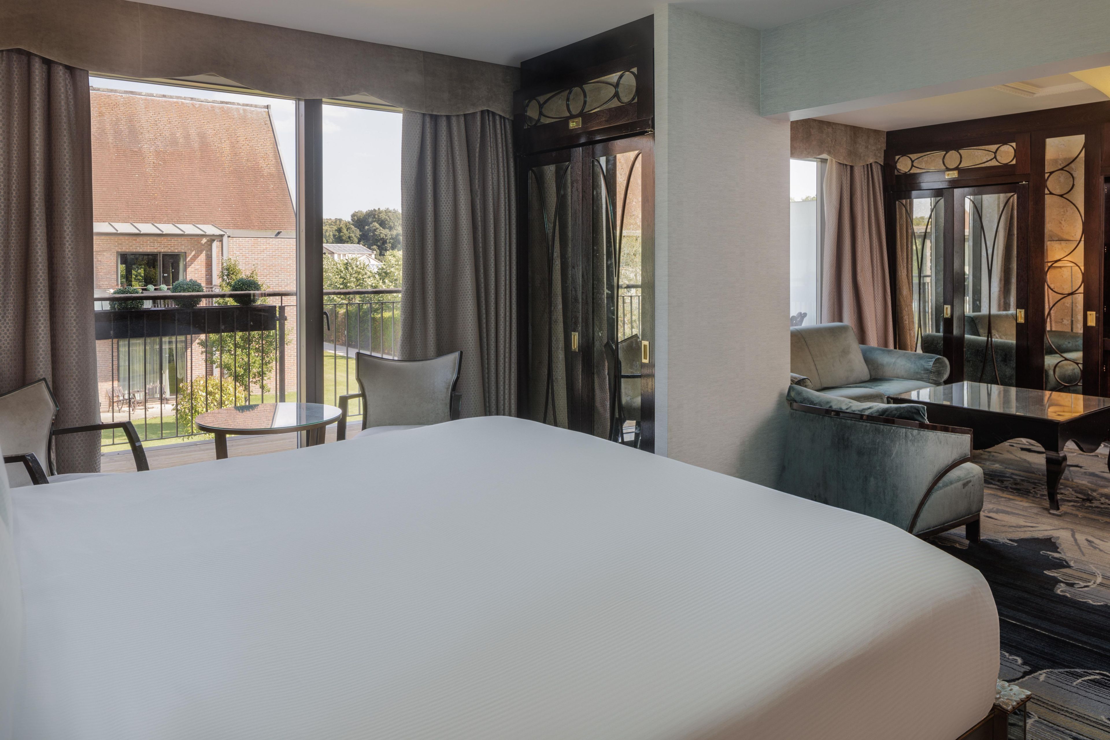 Habitación de hotel con una cama grande, una mesita, dos sillas y un balcón con vistas al exterior.