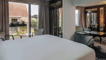 Habitación de hotel con una cama grande, una mesita, dos sillas y un balcón con vistas al exterior.