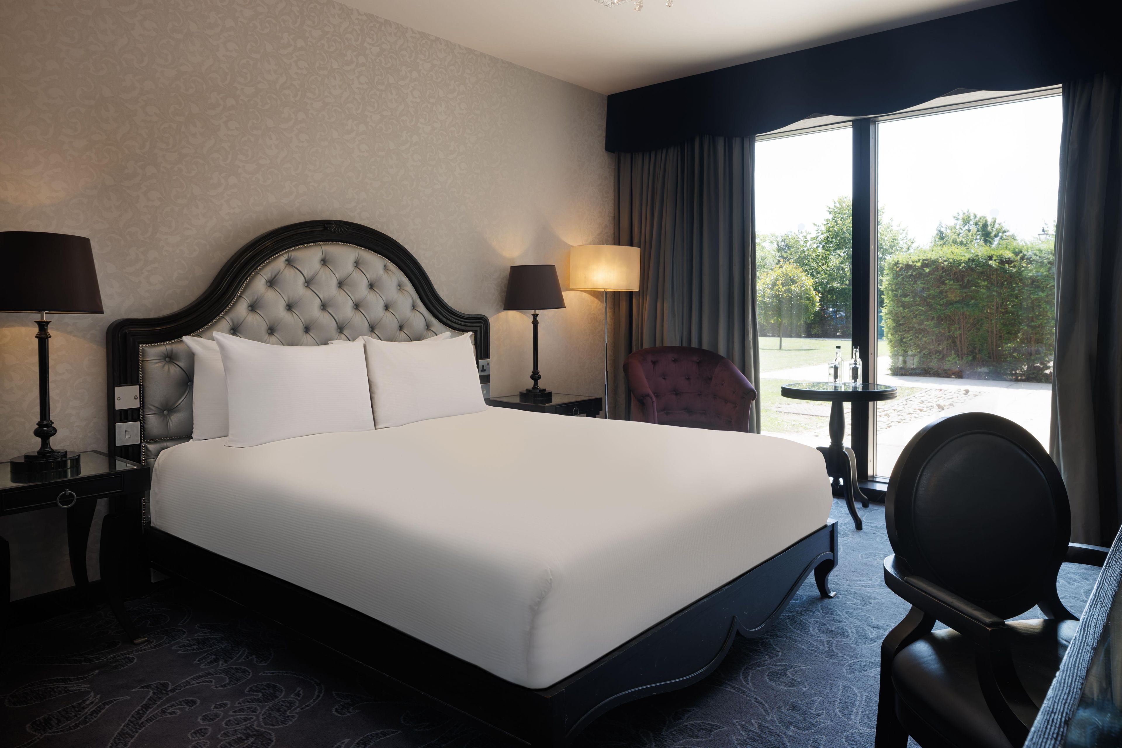 Une chambre d’hôtel avec un grand lit, deux tables de chevet, une chaise et une vue sur l’extérieur.