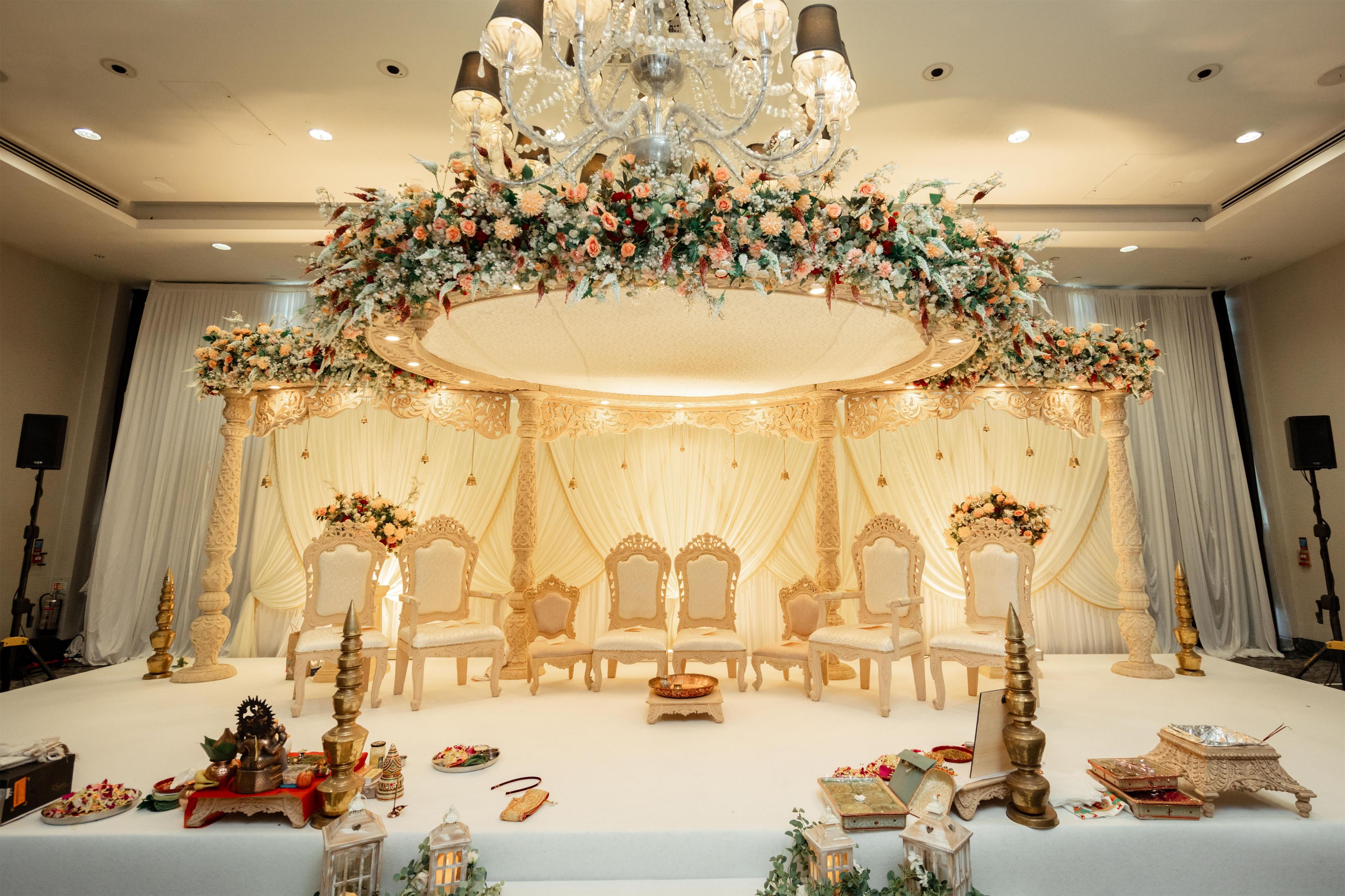 An ornate stage with a floral arrangement, chandeliers, and white draped curtains.