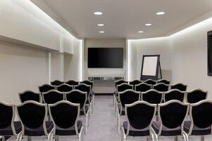 Un salón de conferencias con filas de sillas, un televisor de pantalla plana grande y una pizarra.