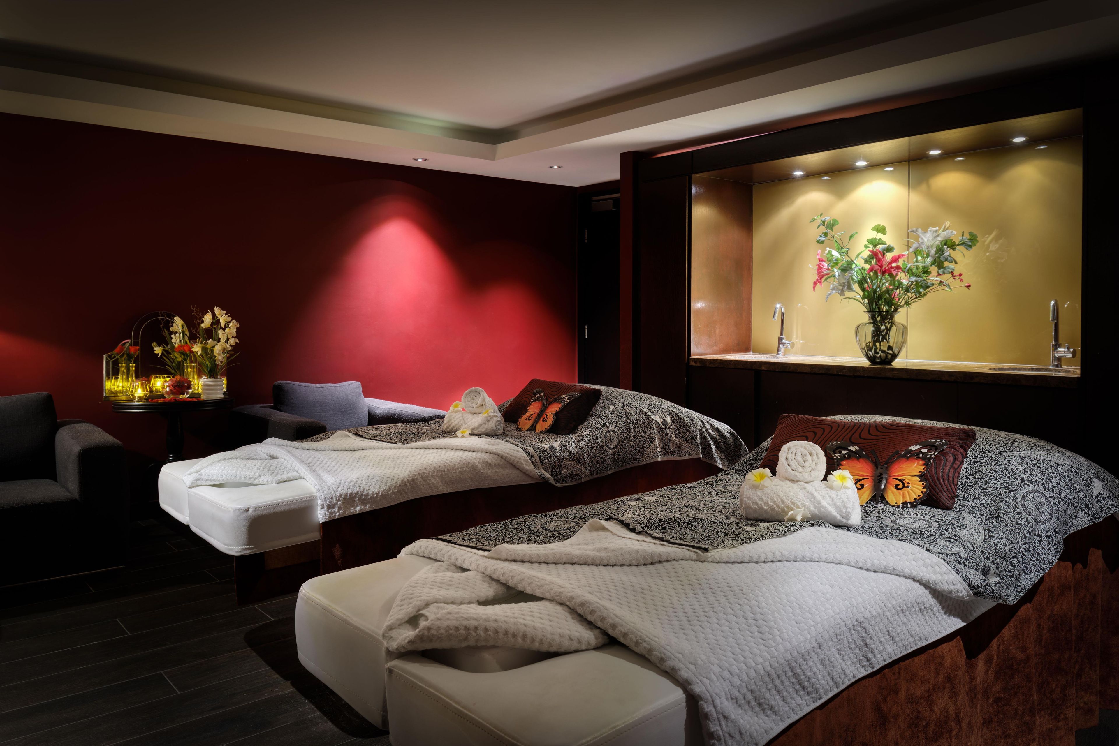 A hotel room with two beds, a sofa, a small table with a lamp, and a window with a view of flowers.